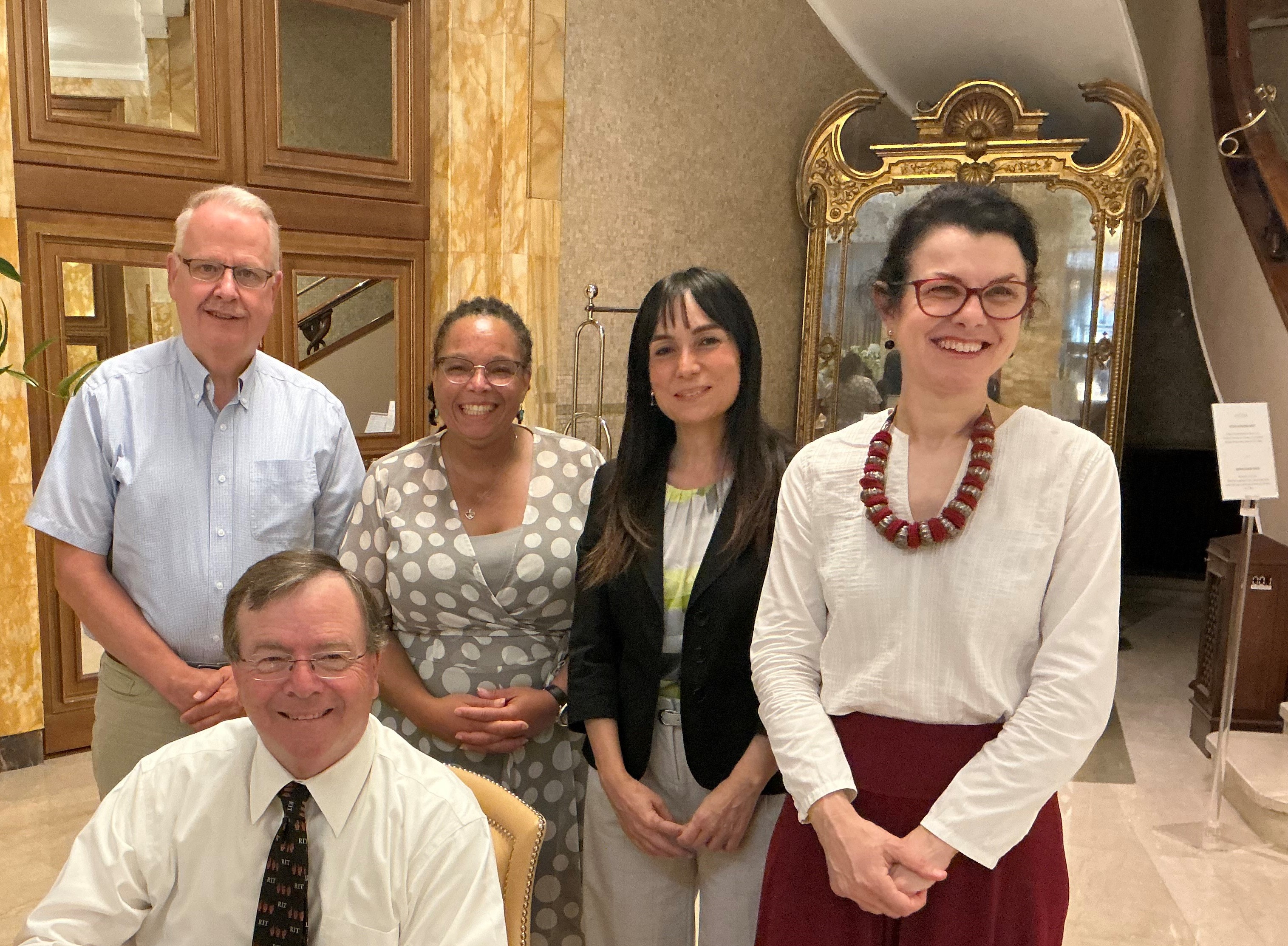 A group of people stand behind Gerry Buckley as he signs paperwork on a desk. They are all smiling. 